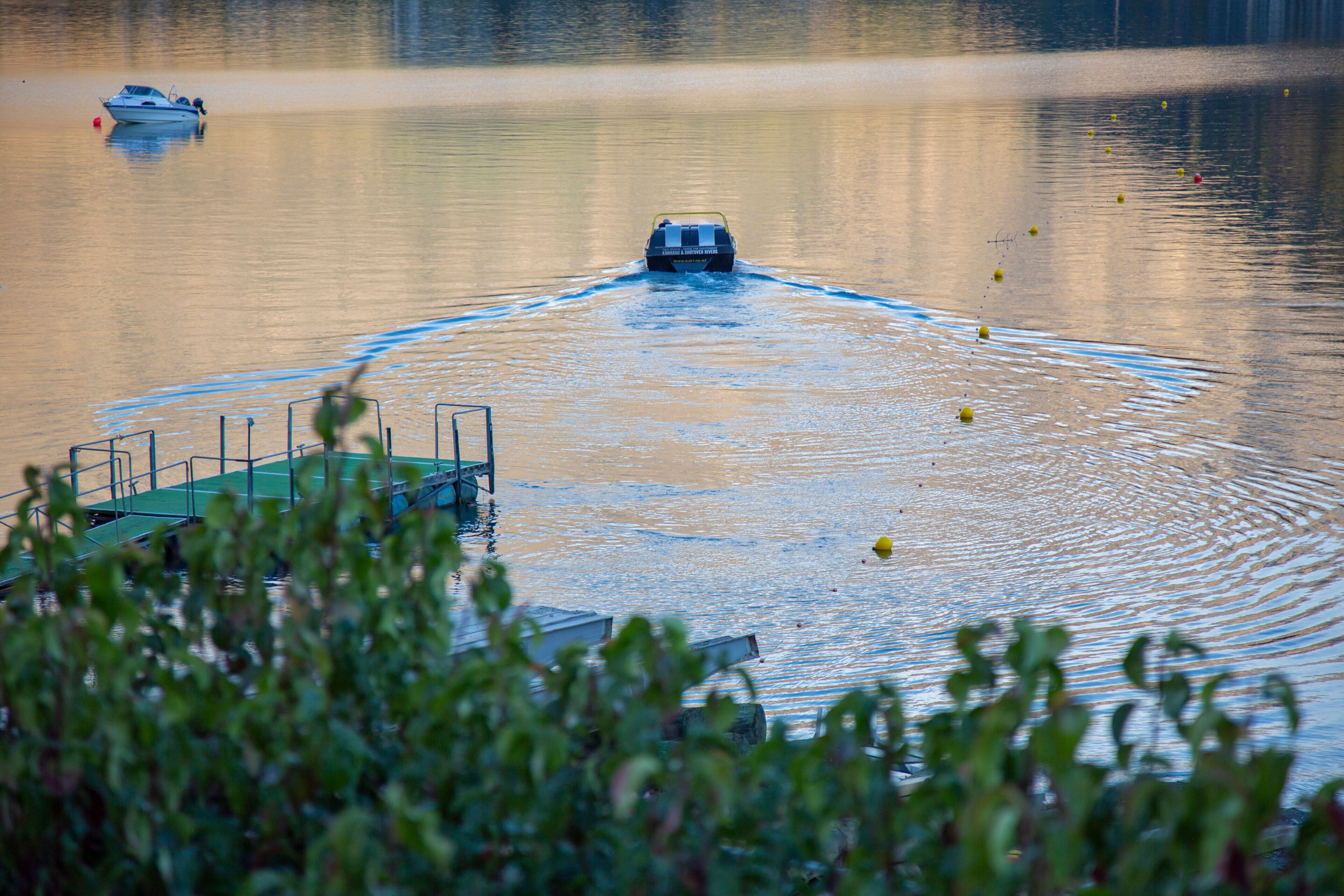 Un bateau navigue sur un lac calme, avec un quai visible au premier plan.
