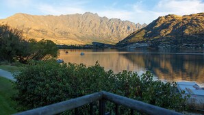 A mountain landscape with a lake, a boat, and a path leading to the water. - Marina 2 Bdrm Apartment with Views (Frankton)