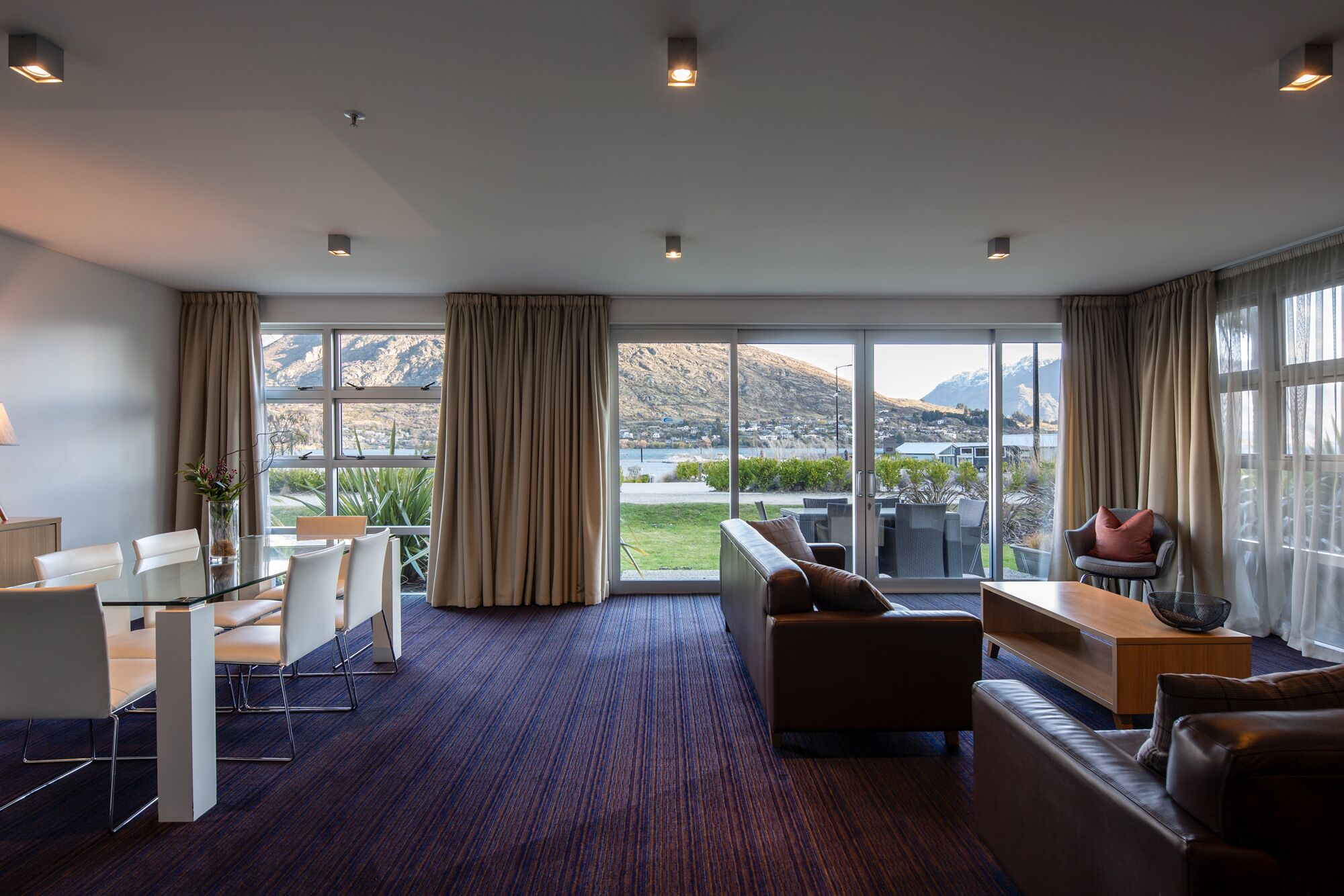 A modern hotel room with a large sliding glass door leading to a balcony with a mountain view.