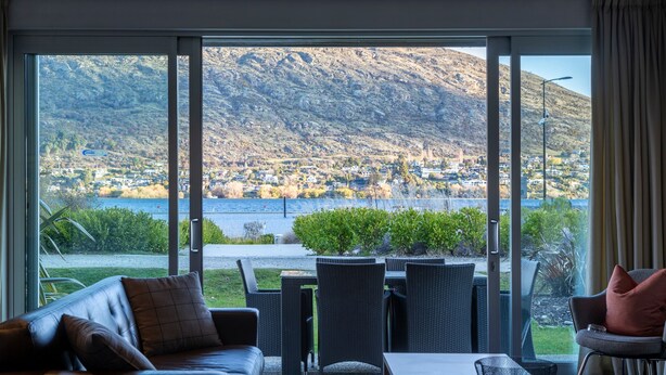 A modern living room with a large window overlooking a mountainous landscape and a lake. - Marina 2 Bdrm Apartment with Views (Frankton)