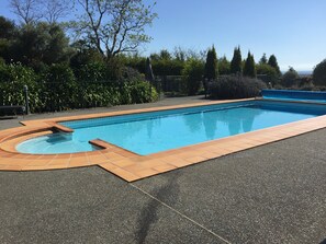 A rectangular swimming pool with a tiled edge, surrounded by a paved area and various plants. - Ambury House - private garden resort with views (Havelock North)