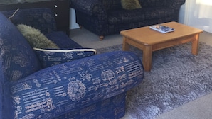 Een woonkamer met een blauwe gestreepte bank, een kleinere blauwe fauteuil, een houten salontafel en een grote spiegel aan de muur.