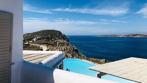 A coastal view with a swimming pool, a rocky hillside, and a clear blue sky. - Villa Savannah (Mykonos)
