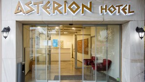 Exterior del Hotel Asterion con una entrada moderna, puertas de vidrio y una zona de recepción visible a través del cristal.