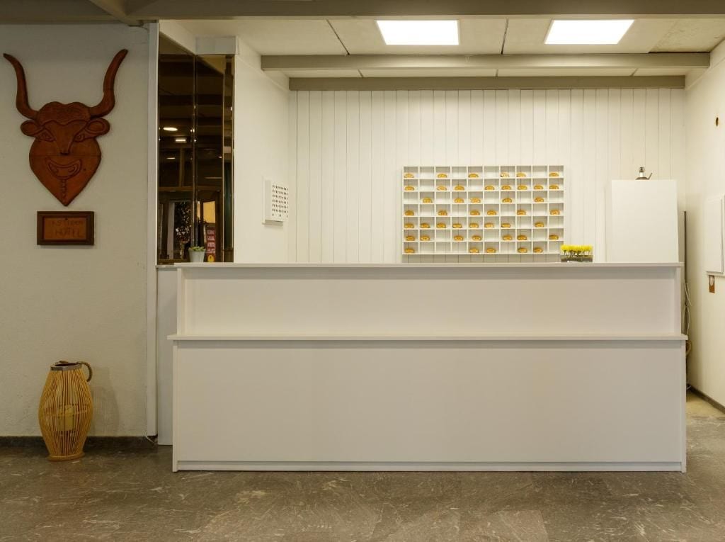 A reception desk with a white counter, a bull head decoration, a wall-mounted shelf with items, and a wicker basket on the floor.