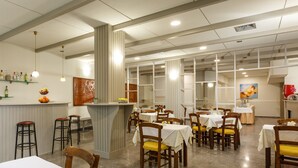 Un restaurante con techos altos, iluminación colgante y una zona de bar central. Las mesas están dispuestas para comer, y hay taburetes cerca de la barra.