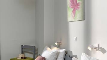Ein modernes Hotelzimmer mit einem Einzelbett, einem Sessel, einem kleinen Tisch mit Lampe und einem Frühstückswagen mit Croissants und Saft.