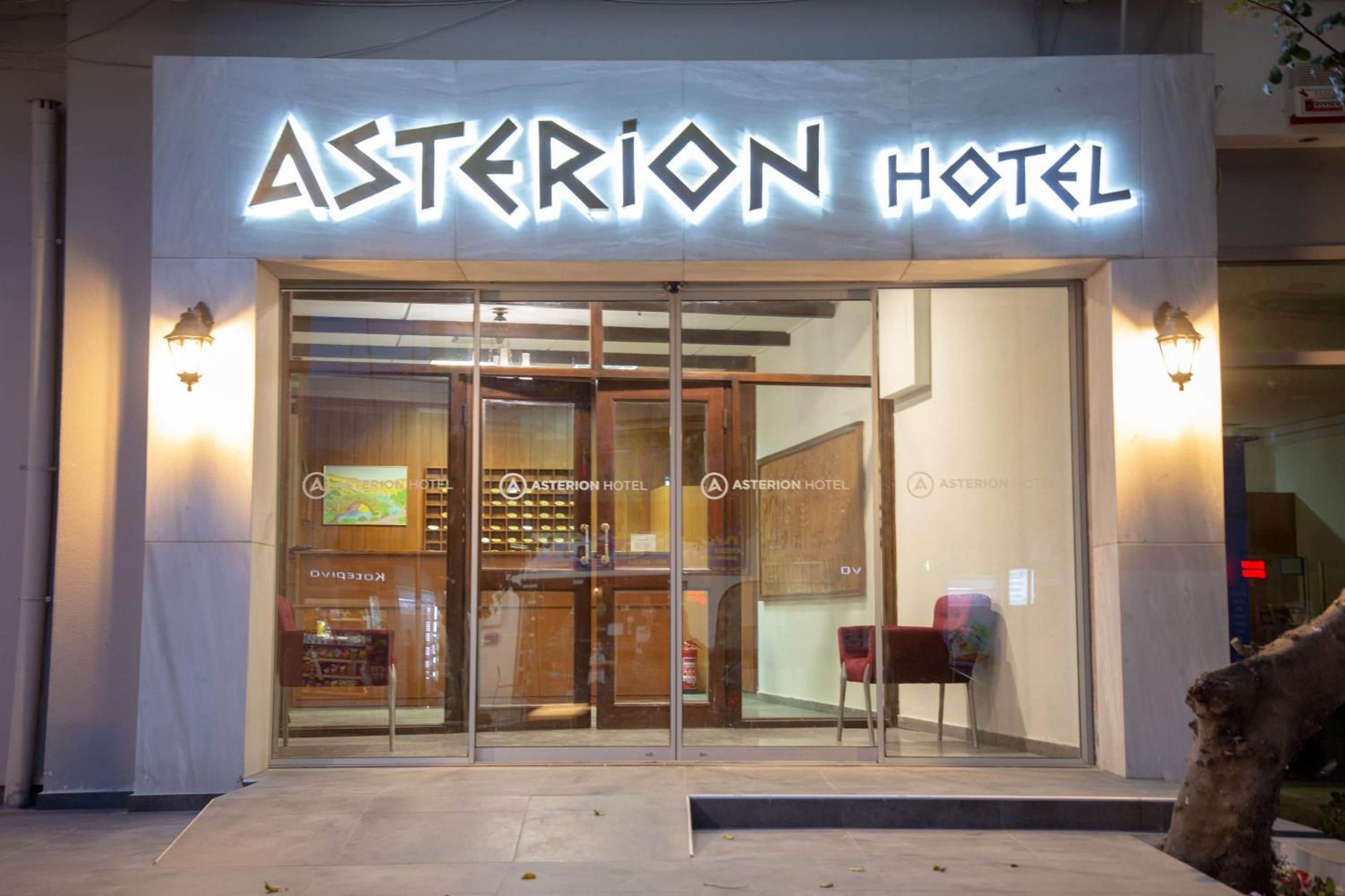 The exterior of the Asterion Hotel with a glass entrance and illuminated signage.