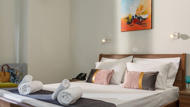 Una cama bien hecha con toallas enrolladas, un cuadro en la pared y una lámpara de noche.