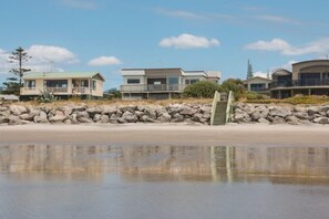 Een strandpand met een modern huis, een trap naar een balkon en een rotsachtige kustlijn.