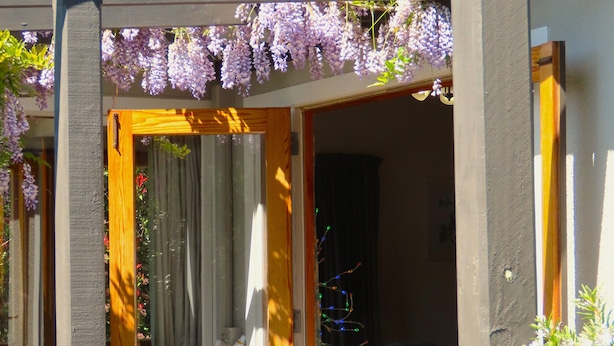 Un patio al aire libre con una mesa y sillas de madera, una botella de vino y una guirnalda de luces.