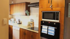 Cocina compacta con armarios de madera, microondas integrado y lavavajillas.