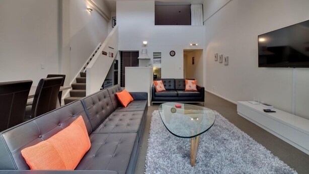 A modern living room with a sofa, a glass coffee table, and a TV mounted on the wall. - Fantastic Cuba apartment (Wellington CBD)