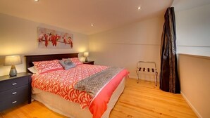 A bedroom with a wooden floor, a bed with red and white bedding, a nightstand with a lamp, and a painting on the wall. - Fantastic Cuba apartment (Wellington CBD)