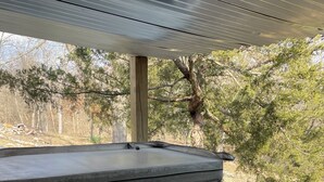A hot tub with a control panel, surrounded by a wooden deck and trees.