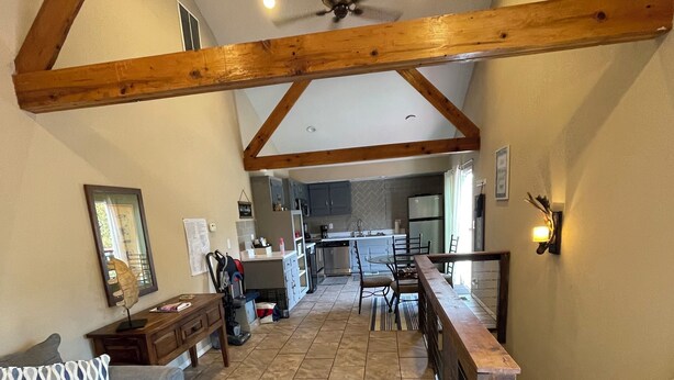 A spacious living area with a high ceiling, wooden beams, a dining table, a sofa, and a kitchen in the background.