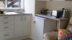 Una cocina compacta con un lavamanos, un refrigerador pequeño y una encimera con una tostadora y una tetera.
