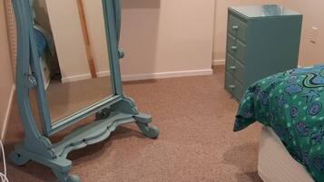 A bedroom with a bed, a dresser, and a mirror on a carpeted floor.