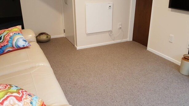 Una habitación con alfombra color crema, una pizarra en la pared, una puerta y un televisor montado en la pared.