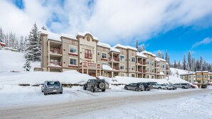 A multi-story hotel with a snow-covered exterior, parking lot, and surrounding trees.