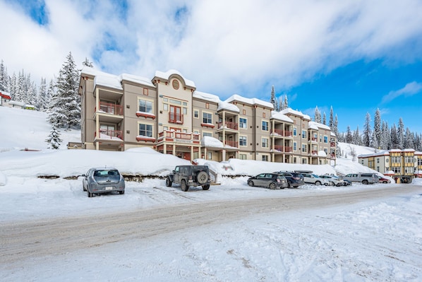 A multi-story hotel with snow-covered balconies and a parking lot with several cars.