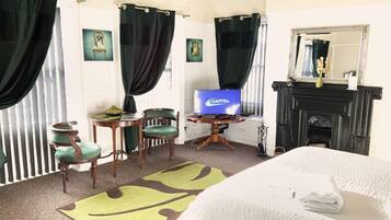 Una habitación de hotel con una cama, televisión, chimenea y una silla verde.