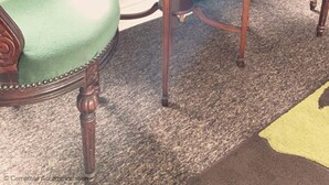 A room with a round wooden table, two green upholstered chairs, a green curtain, and a carpeted floor.