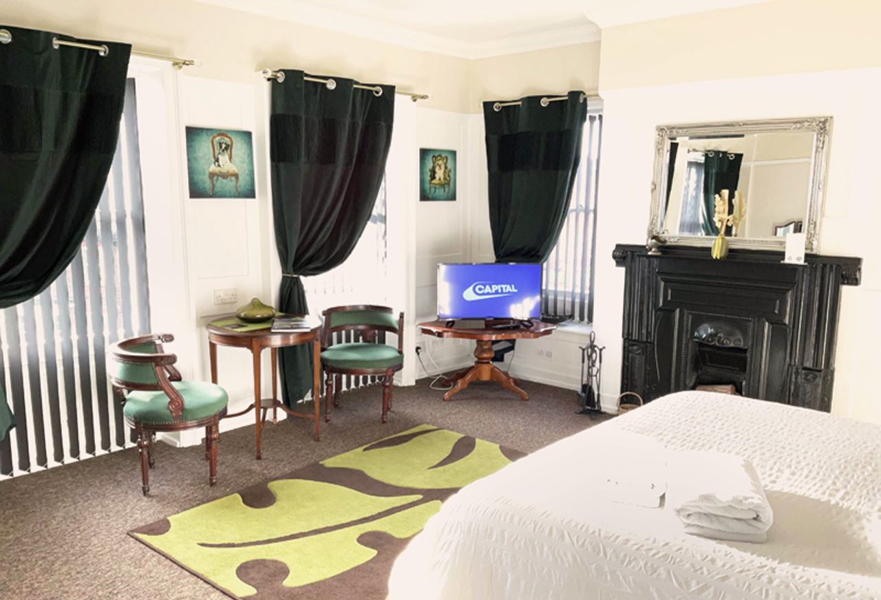Une chambre d’hôtel avec un lit, une télévision, une cheminée et un fauteuil vert.