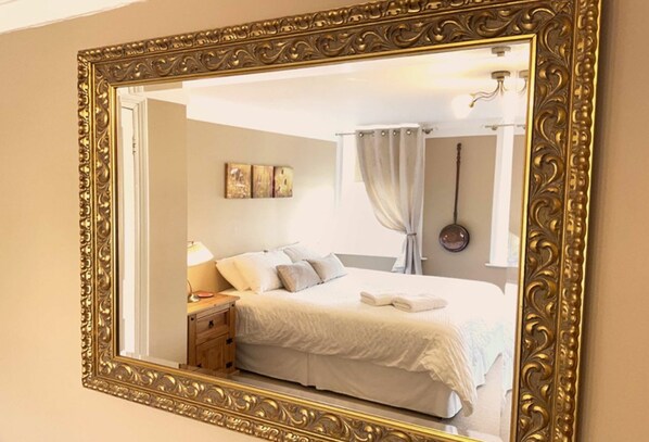 Camera da letto con un grande specchio decorativo, un letto con lenzuola bianche, un comodino con una lampada e un'opera d'arte appesa al muro.