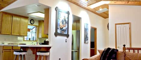 A spacious living area with a wooden ceiling, a kitchen with wooden cabinets, and a dining area with stools.