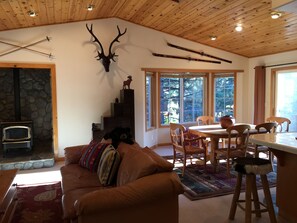 A cozy living room with a stone fireplace, a wooden ceiling, and a dining area with a table and chairs.