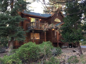 A wooden cabin with a balcony, surrounded by trees and shrubs.