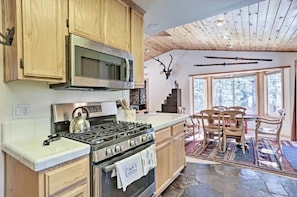A kitchen with wooden cabinets, a stove, and a microwave. There is a dining area with a table and chairs.