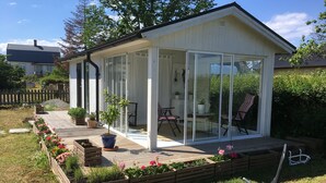 A small, white, glass-enclosed patio area with a wooden deck, potted plants, and outdoor furniture.