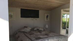 A bedroom with a wooden ceiling, a bed with a patterned quilt, a wall-mounted TV, and a framed picture.