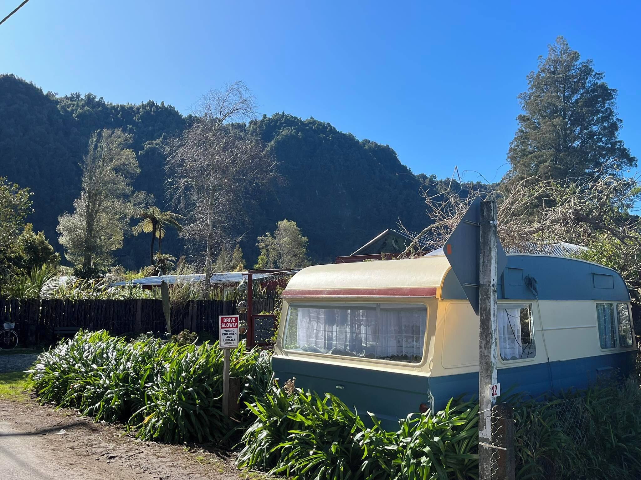 A vintage camper parked in a lush, green area with a mountainous backdrop.