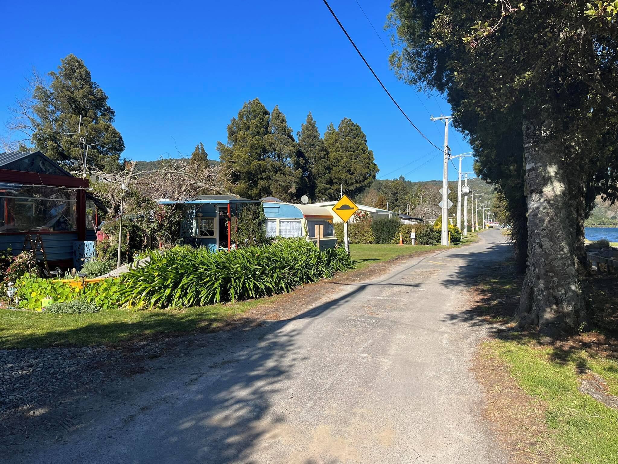 Une route de campagne, avec des maisons d’un côté et une étendue d’eau de l’autre.