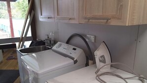 Cozinha compacta com máquina de lavar, pia e armários de madeira.