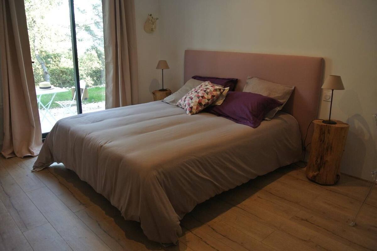 Een slaapkamer met een groot bed, twee nachtkastjes met lampen, een raam met gordijnen en uitzicht op de omgeving.