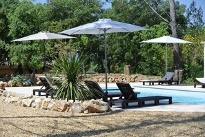 Ein Poolbereich mit Liegestühlen und Sonnenschirmen, umgeben von Felsen und Pflanzen.