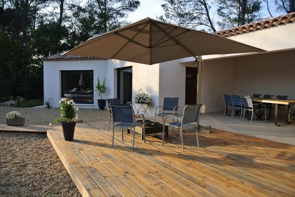An outdoor patio with a wooden deck, a table with chairs, and a large umbrella. - Villa Carpe Diem (Lorgues)