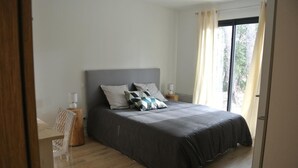 Une chambre avec un grand lit, une table de chevet, une chaise et une fenêtre avec des rideaux.
