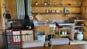 A rustic kitchen with a wood stove, shelves with jars and bottles, and a sink. - Riverside Retreat   (Waimakariri District)