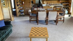 A cozy wooden interior with a dining table and chairs, a fireplace, and shelves with various items. - Riverside Retreat   (Waimakariri District)