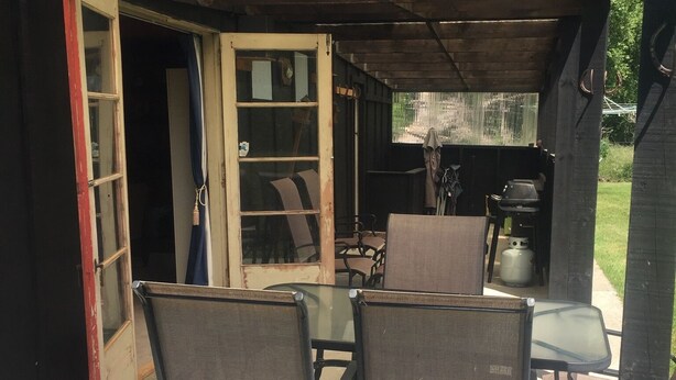 An outdoor patio with a table and chairs, a grill, and a covered area with a door leading to a room. - Riverside Retreat   (Waimakariri District)