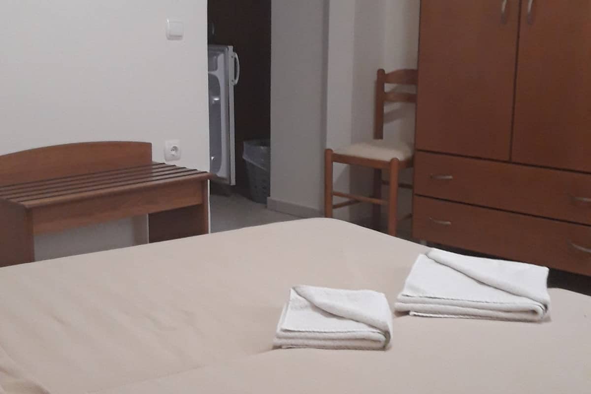 A bedroom with a bed, a wooden chair, a wardrobe, and a white air conditioning unit.