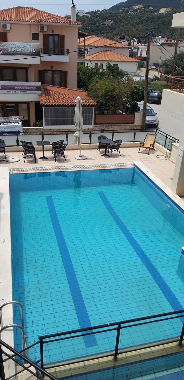 A swimming pool with tiled flooring, surrounded by outdoor furniture and a railing. - Dabasis-Drolias (Skiathos)