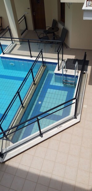 A swimming pool with a glass barrier and metal railings, a door with a number, and a small table with chairs.