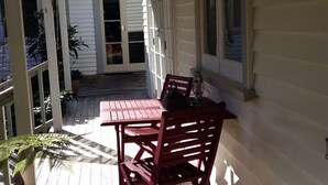 Een overdekte veranda met een houten tafel en stoelen, plantenpotten en een schuifdeur die leidt naar een overdekt terras.