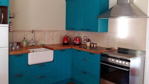 Een keuken met blauwgroene kastjes, een roestvrijstalen afzuigkap, een spoelbak en een fornuis.